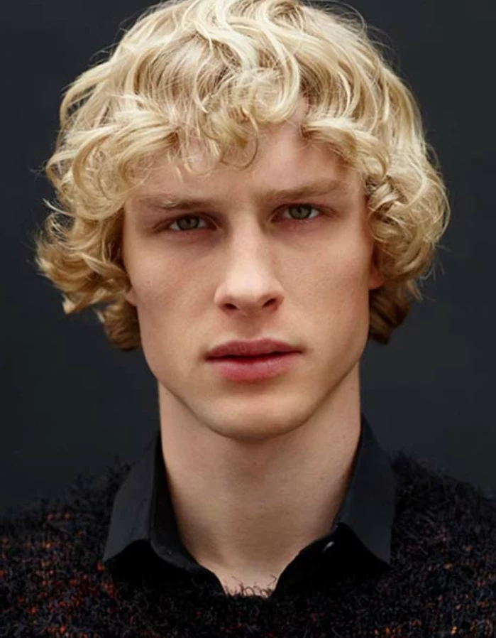 curly shaggy light blonde hair, long hairstyles for boys, worn by blue-eyed man, in black shirt, and black and red jumper