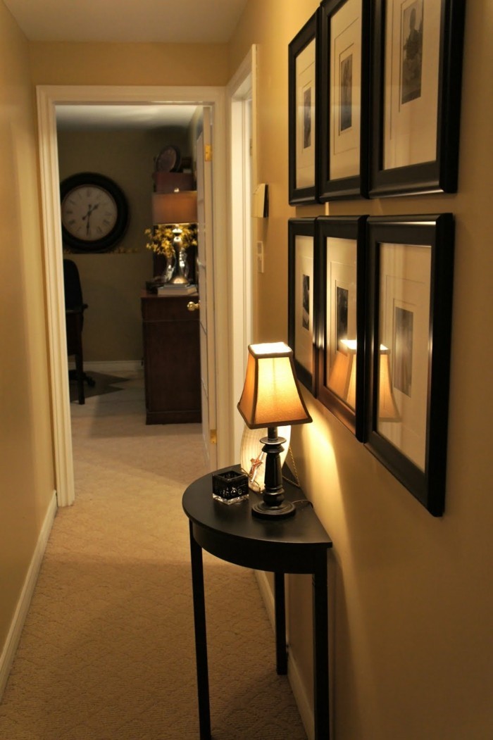small black table, with lit table lamp, six small images in black frames, arranged in two rows, hallway furniture ideas, pale beige walls and carpet 