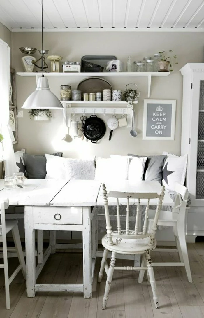 several cushions in dark grey and white, on shabby chic sofa, near a white, antique kitchen table, with matching chairs