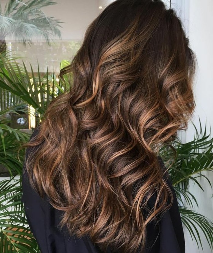 honey blonde highlights, in dark brown curled hair, brunette hair colors, worn by woman in black top or robe, green ferns in background