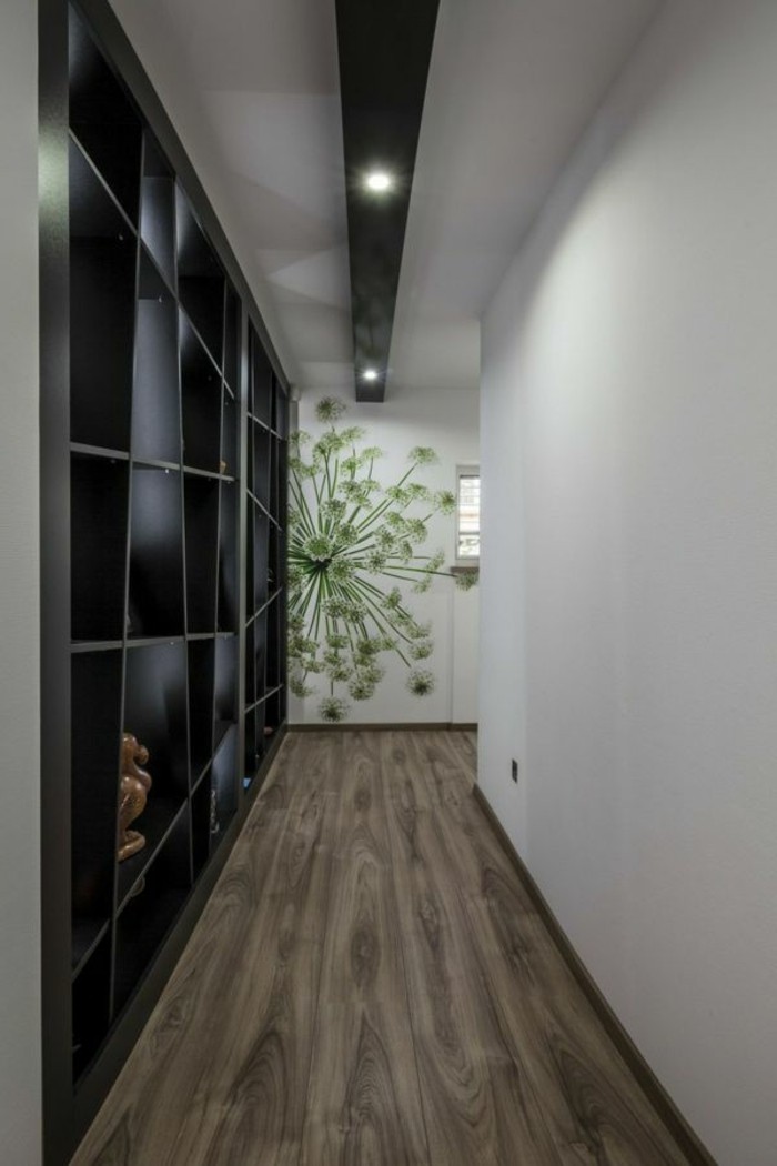 black asymmetrical shelves covering a wall, in corridor with wooden floor, opposite wall is plain white, third wall has a green floral mural, hallway furniture ideas