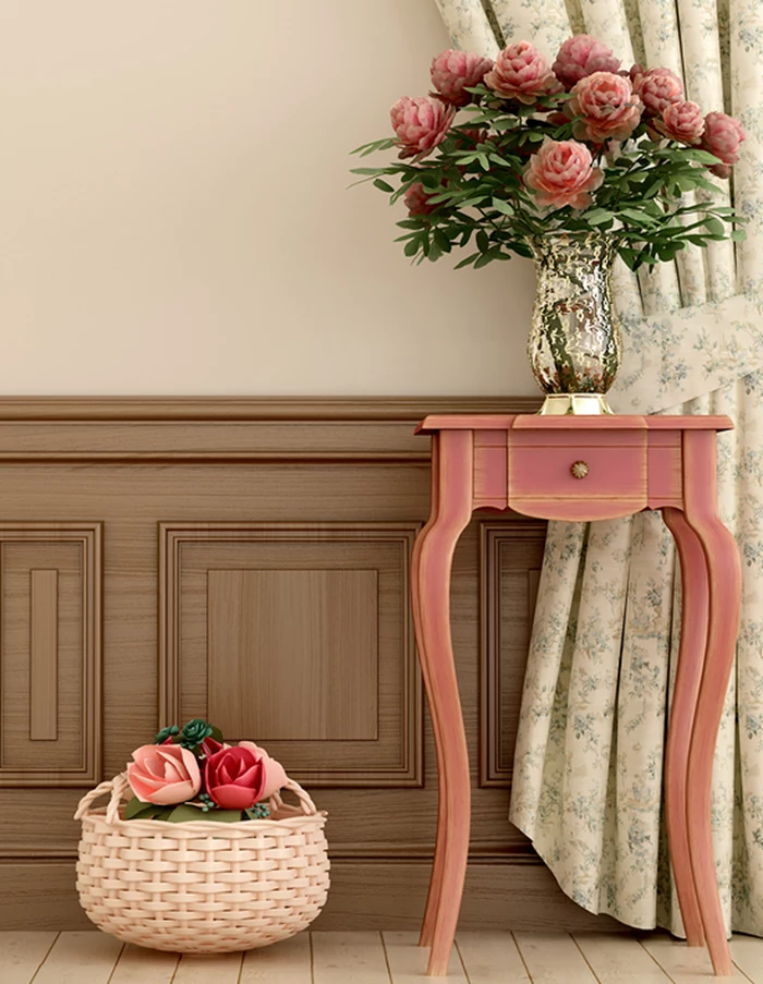 digital 3D illustration, depicting pale beige wall, with wooden paneling, coral pink antique table, with small drawer, and a shiny vase containing pink flowers