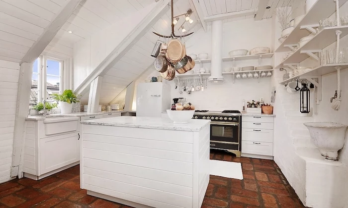 white kitchen with rough brown tiled floor, wooden kitchen island painted in white, shelves with various utensils, shabby chic decorating 