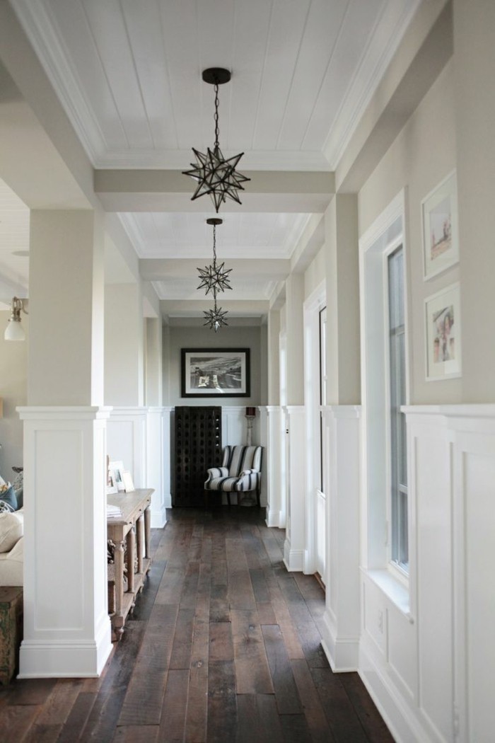black and white star-shaped lamps, hanging from a white ceiling, inside a corridor with pale beige walls, with white paneling, hallway decor ideas, dark solid wooden floor