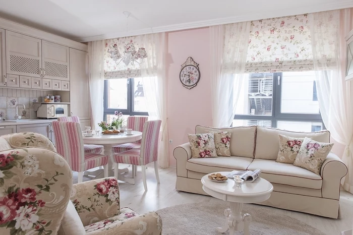 cream shabby chic sofa, with floral cushions, armchair with a matching floral pattern, near white round antique coffee table, in living room with pale pastel pink walls, shabby sheek 
