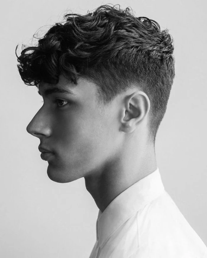 black and white image of a young man, standing in profile, with faded haircut, and curly quiff, wearing white shirt, cool haircuts for boys