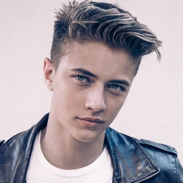 young man with blonde hair, styled in a textured quiff, with deep side part, boys short haircuts, he is wearing a white shirt and leather jacket