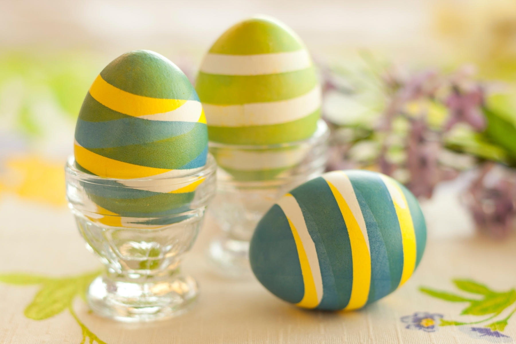 striped eggs in different shades of green, with white and yellow, how to dye easter eggs, two in clear glass dishes, one placed on the table