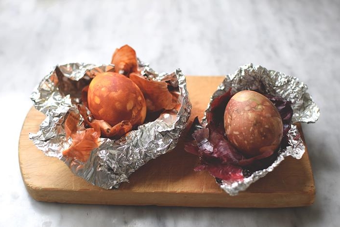 massive wooden board, containing tin foil, with two eggs, dyed in natural brown and orange, next to onion peels, easter egg ideas for coloring