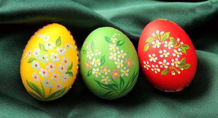 simple white and orange flowers, with green leaves, painted on easter eggs, dyed in red green and yellow