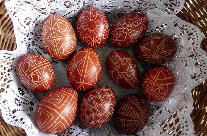 wax decorated eggs, dyed in red, and featuring complex, symmetrical geometric patterns, easter egg coloring, placed on a white doily, in a wicker basket