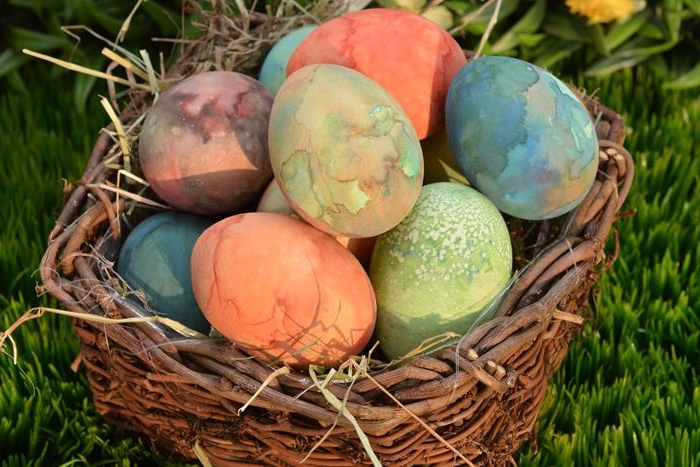 watercolor effect spotty eggs, in orange and green, blue and pink, easter egg coloring techniques, placed in a basket made of twigs