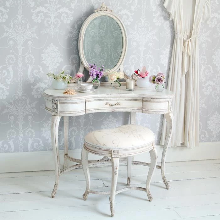 vanity in antique french style, painted in white, and featuring an oval mirror, and a matching stool, shabby chic decorating, different flowers in vases and cups