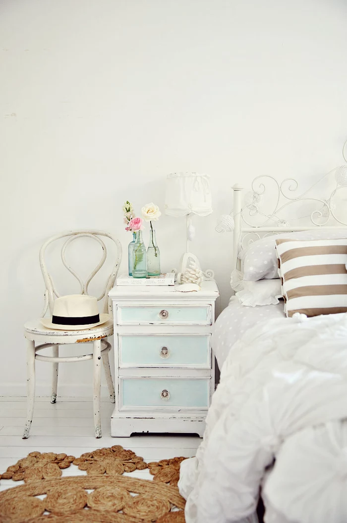 shabby chic furniture, vintage chair with white chipping paint, antique pale blue and white cupboard, bed with white wrought-iron frame, and soft white bedding