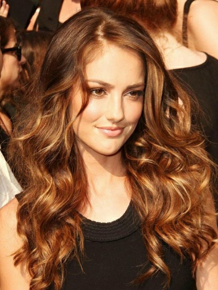 frizzy and messy, curled and side-parted hairstyle with layers, on medium length brown hair, worn by smiling woman, with discreet make up, and black sleeveless top