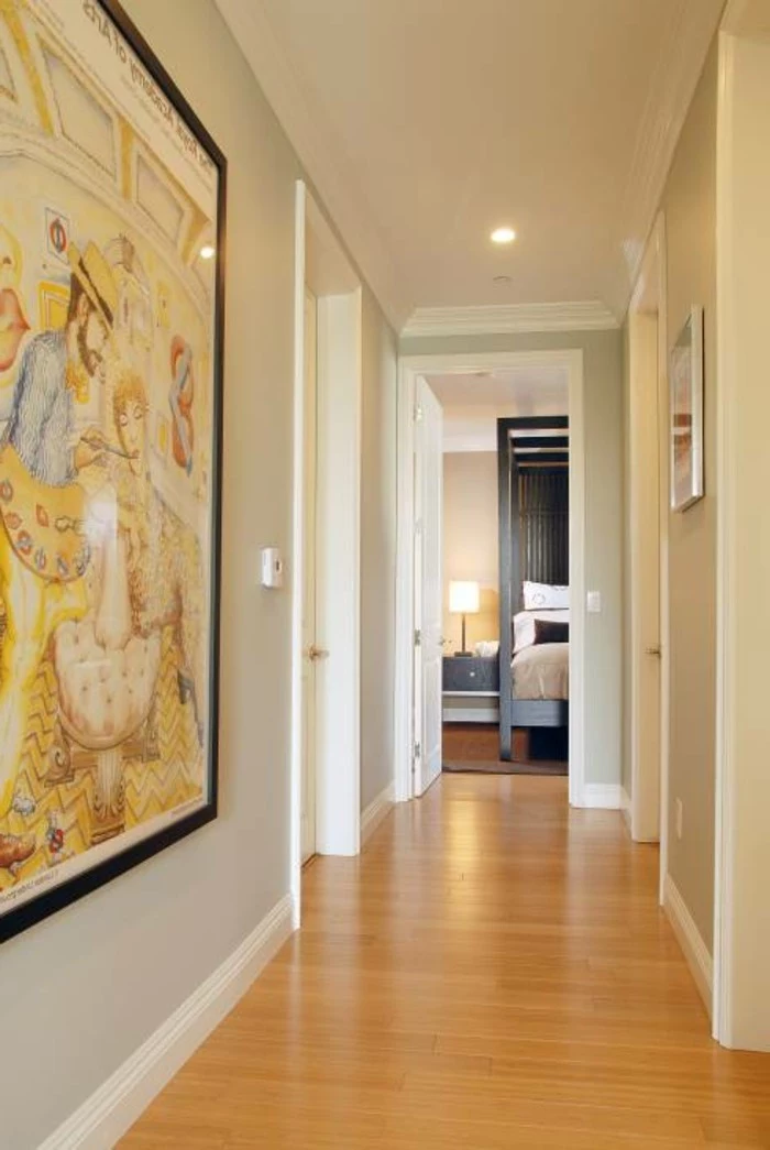 warm pale orange laminate floor, inside a corridor with pale grey walls, and white doors, large framed artwork on one wall
