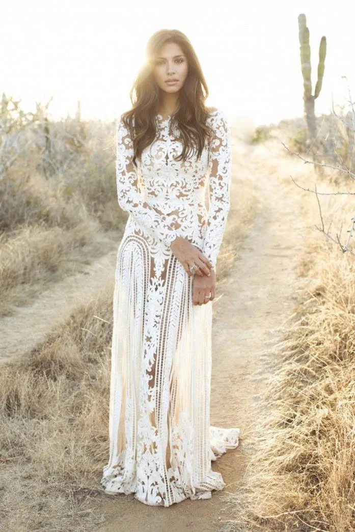cutout white lace wedding dress, boho fashion gown, worn by brunette woman, with long wavy hair, standing on a desert road