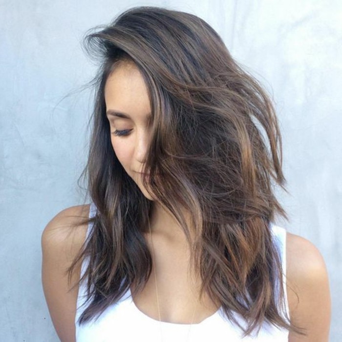 nina dobrev in white tank top, with side swept wavy hair, in medium brown hair color, with dark blonde highlights