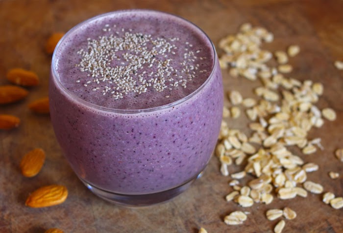 tiny seeds topping a small glass, filled with a blended purple drink, fruit smoothie recipes, raw almonds and oatmeal flakes nearby