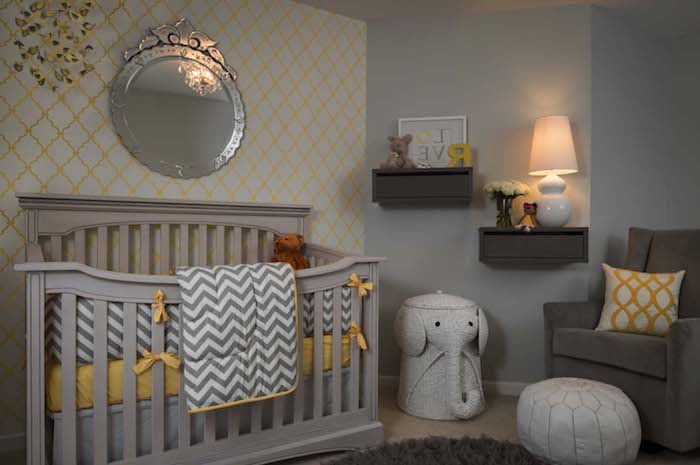 baby nursery, in gray and yellow, with creamy light gray crib, large ornate wall mirror, dark gray armchair, white and yellow cushion, and other yellow details