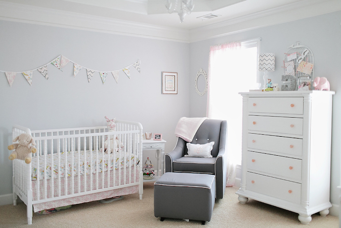 dark gray armchair, and matching footstool, near baby crib in white and pale pink, and matching chest of drawers, baby girl room décor, pale lavender walls, toys and decorations
