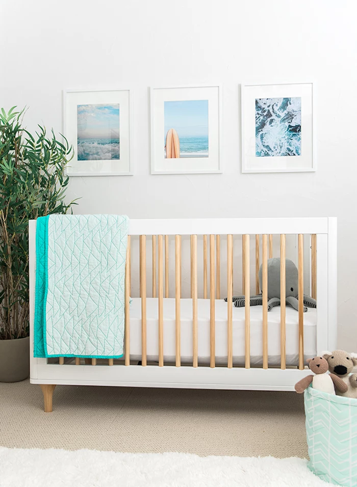 three images in white frames, hanging over white wooden crib, with beige details, gender neutral nursery, large green plant, stuffed gray octopus toy