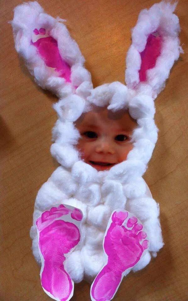 bunny-shaped paper figure, easter crafts for preschoolers, with white cotton balls, and decorated with child's footprints in pink, and a photo of a child's face