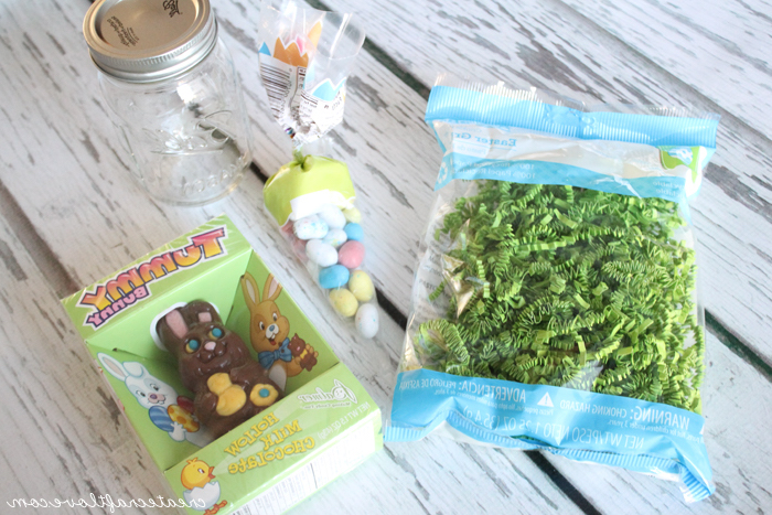 clear glass mason jar, near bag of green paper easter grass, easter projects, packet of small, egg-shaped candy, and a chocolate bunny