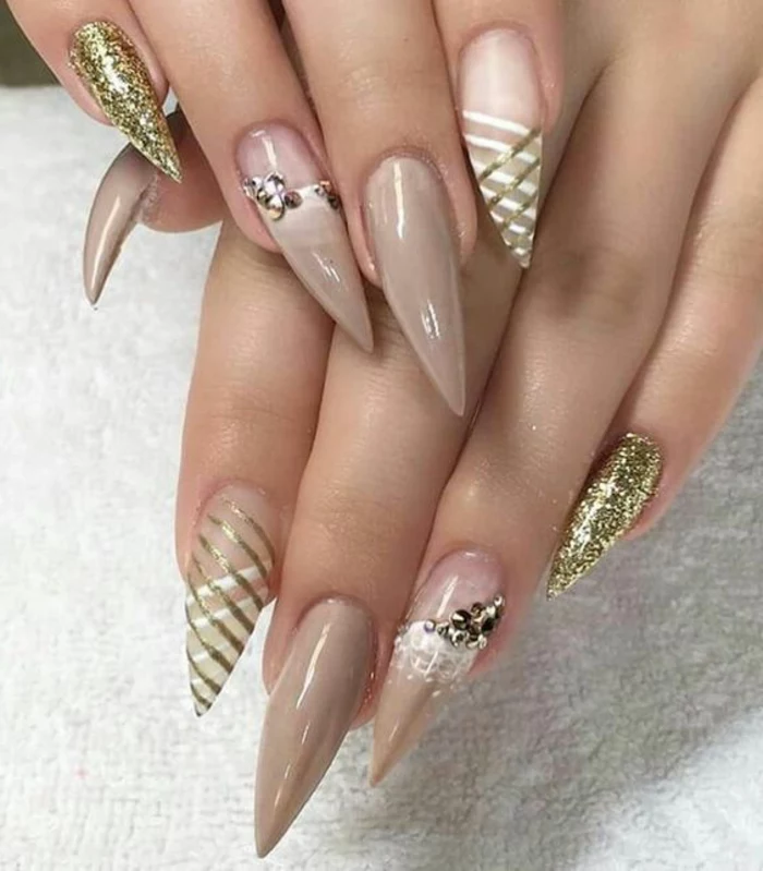very long and sharp stilleto nail designs, painted in nude beige, and clear nail polish, decorated with golden glitter, stickers and hand-painted figures, in white and gold