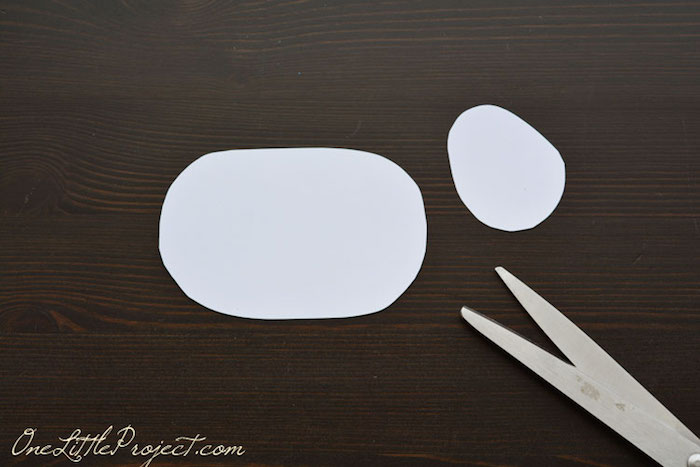 big oval and small, roundish white paper cutouts, easter crafts for kids, on a dark wooden surface, near pair of scissors