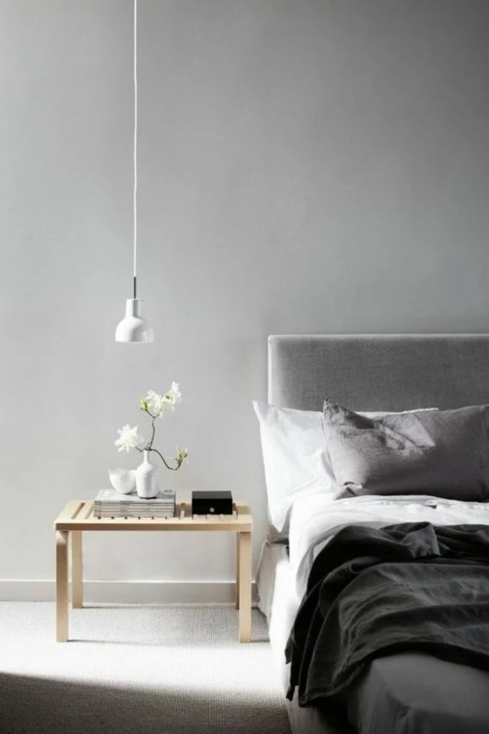 minimalist bedroom, with light gray walls, small wooden bedside table, grey bed with white, light and dark gray bedcovers