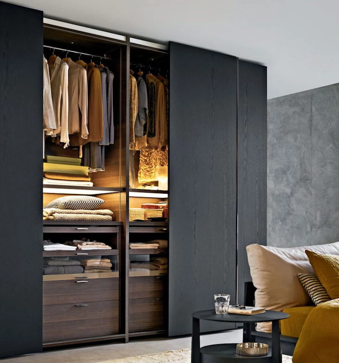 open closet with sliding doors, made of black wood, with clothes and blankets, near bed with black bedside table
