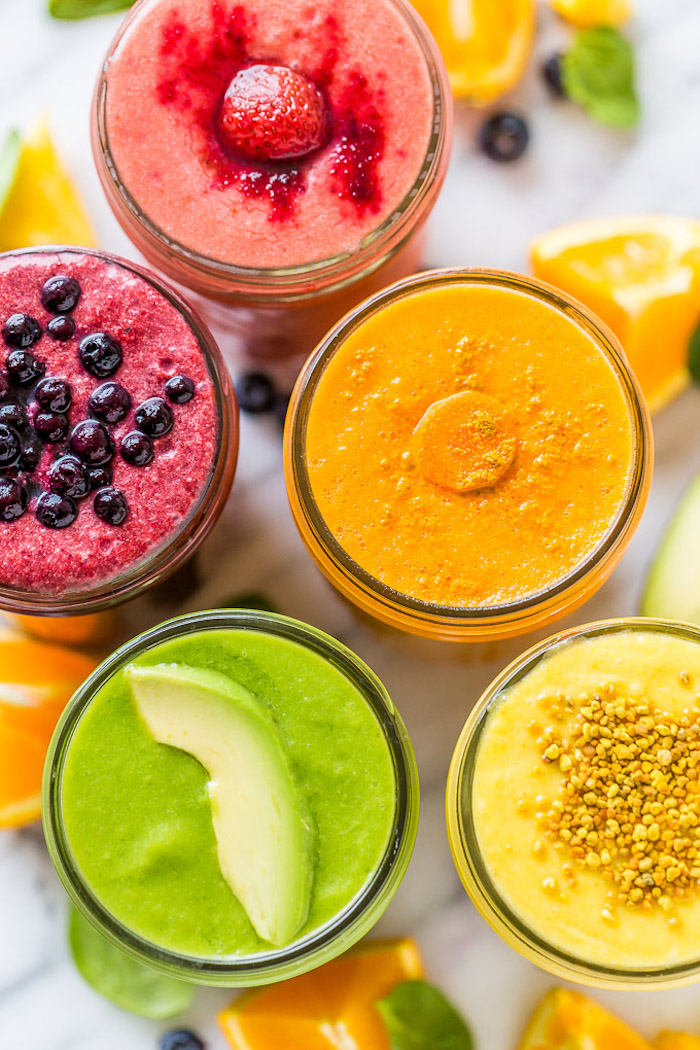 green smoothie recipe, five glasses filled with colorful creamy drinks, made from different fruits and veg, strawberries and blueberries, carrot and avocado