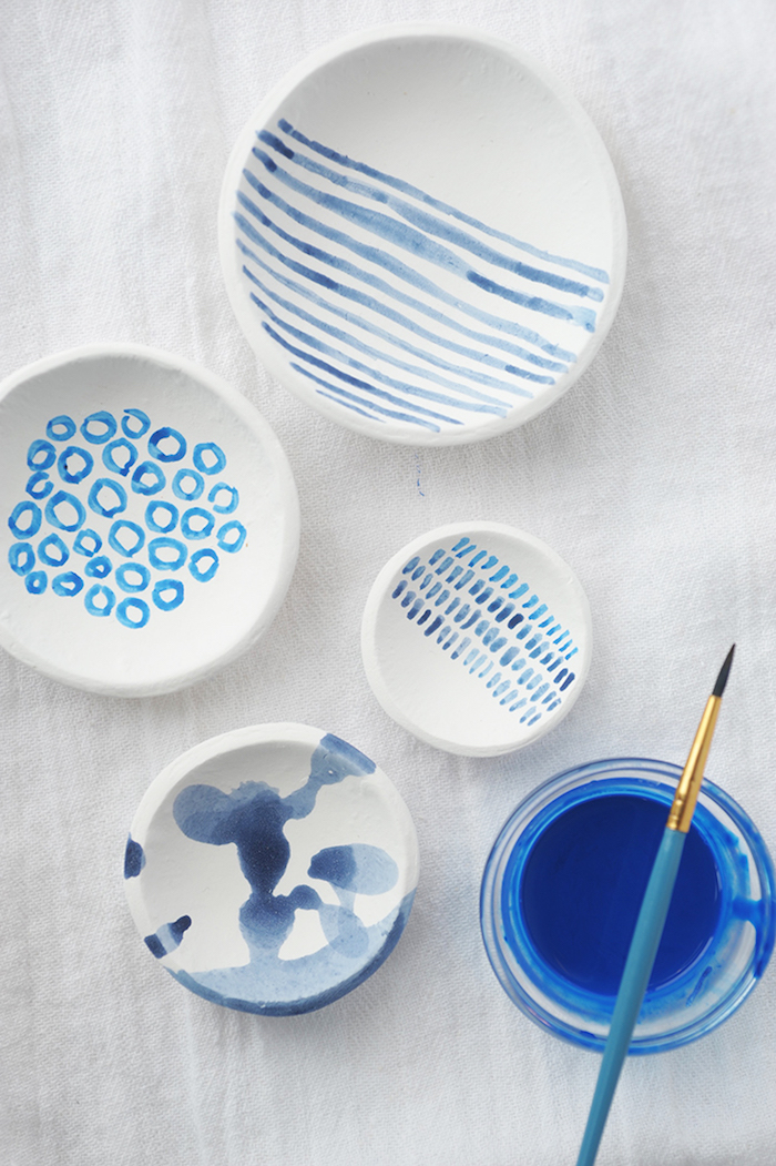 four white plates, decorated with light blue patterns, done in watercolor, mothers day gifts, glass with blue paint, and brush nearby