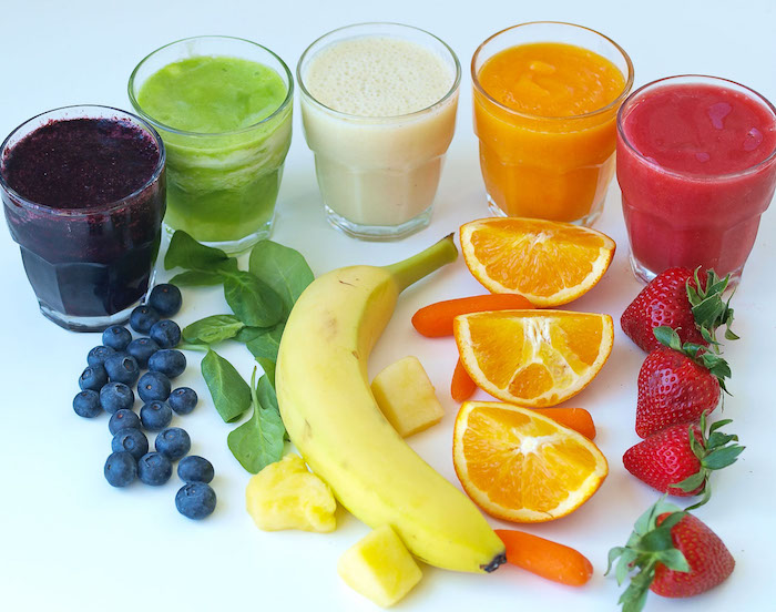 strawberries and oranges, baby carrots and a banana, spinach and blueberries, near five glasses, containing frothy blended drinks, spinach smoothie ideas
