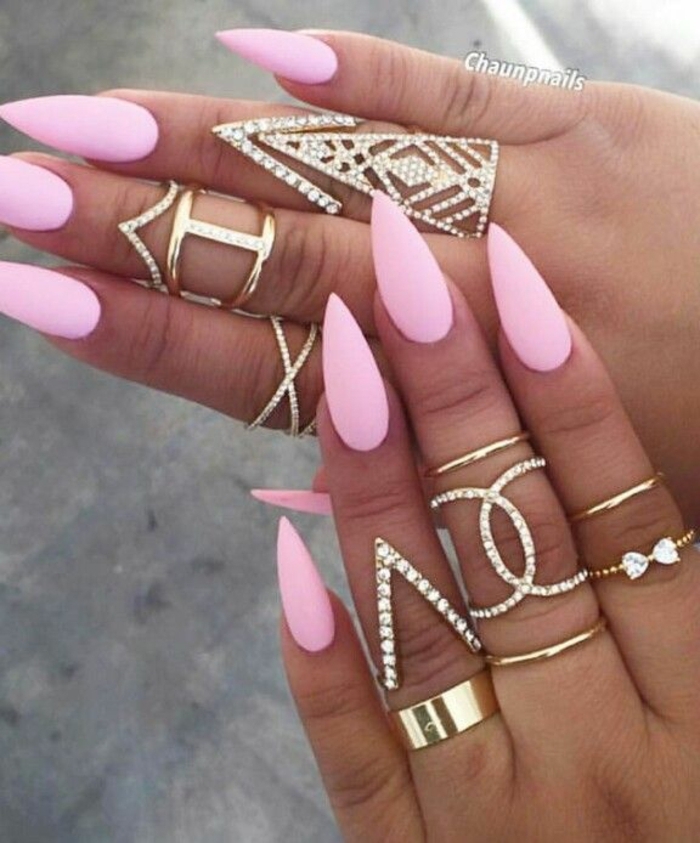 chunky golden rings, some decorated with rhinestones, on two hands, with long manicure, painted in light matte pink nail polish