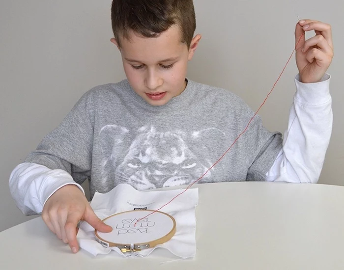 young boy embroidering, with red thread, on white piece of cloth, top 10 mother's day gift ideas, sweet message for mom