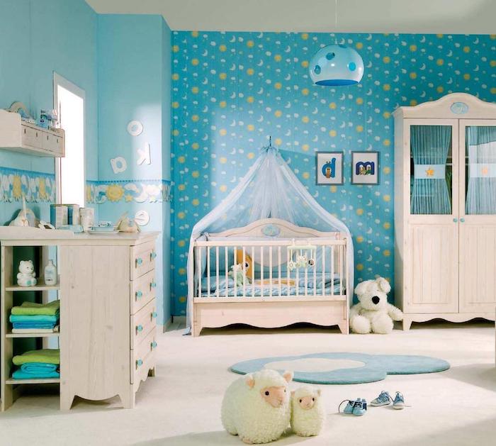 wallpaper in blue, with sun and moon pattern, in boy nursery, with pale beige wooden furniture, clothes and stuffed toys