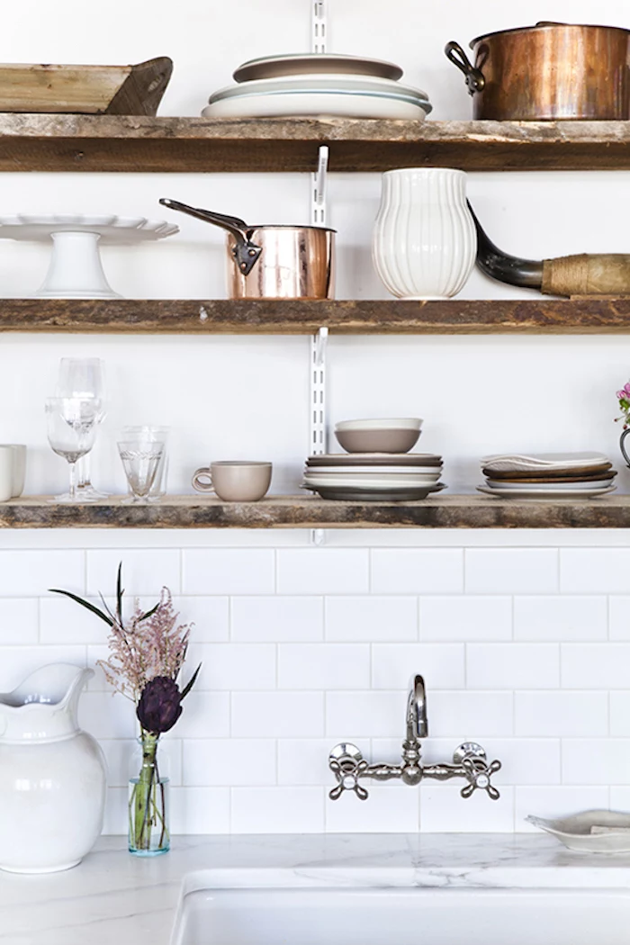 ceramic jugs and plates, and various brass pots, on wooden shelves, suspended over an antique sink, marble-like white and gray surface