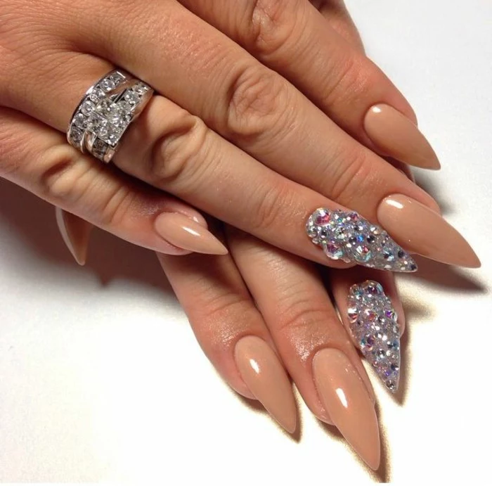 gem nail decal stickers, in many different colors, on manicure with nude beige nail polish, and long stiletto nails, on hand with encrusted silver ring