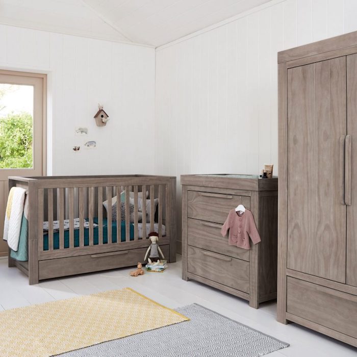 furniture for a nursery, a set of brown baby crib, wardrobe and changing table, baby girl room décor, in white room, with toys and clothes