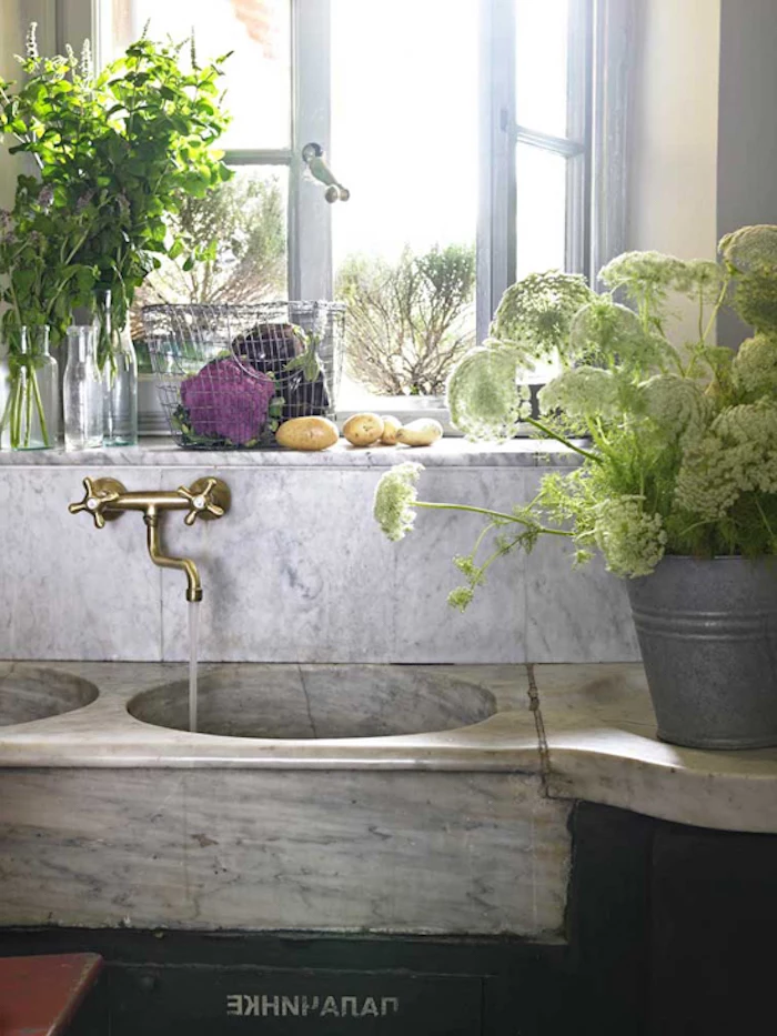 open window next to a stone sink, with retro metal tap, a bucket with flowers, and vases with fresh herbs nearby