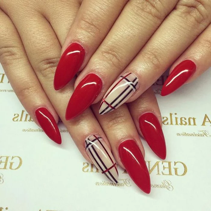 stiletto nails, painted in smooth and bright, shiny red nail polish, accent nails decorated with black, white and red stripes, inspired by burberry
