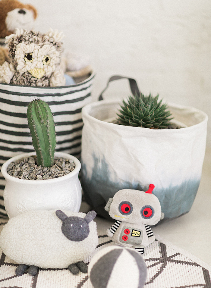 two indoor plants, in ceramic pots, cactus and succulent, bag with stuffed toys, gender neutral nursery, stuffed sheep robot and ball, patterned rug in white and beige