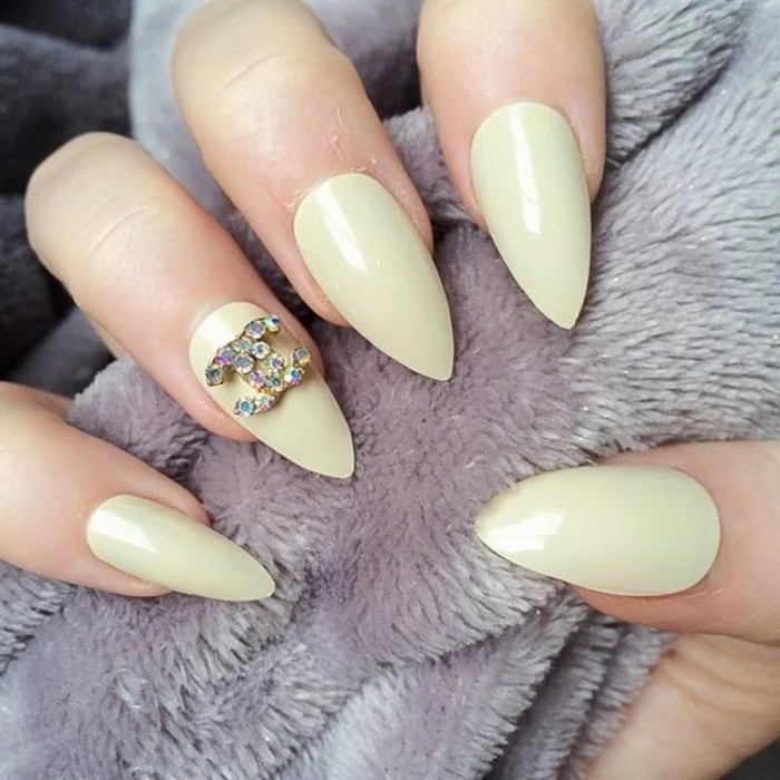 yellowish-green nail color, on sharp pointy manicure, one nail is decorated with chanel logo, covered in iridescent rhinestones
