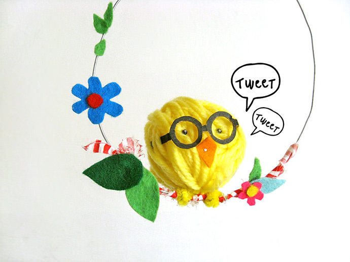 swinging chick ornament, easter crafts for adults, made from yellow ball of thread, with glasses and orange felt beak, stuck to a wire hoop, decorated with felt flowers