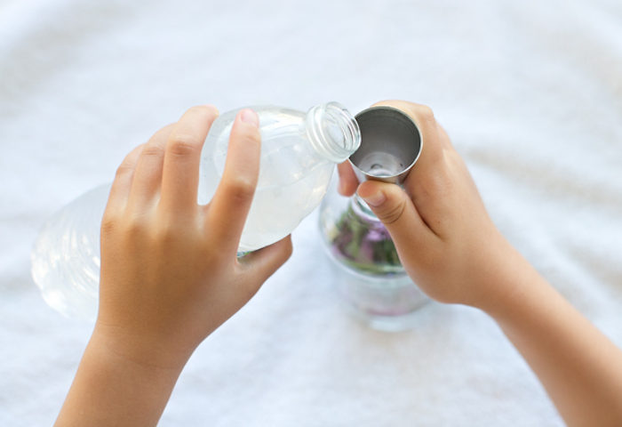 small child hand, pouring water from plastic bottle, into clear bottle with flowers, using metal funnel, mother's day gift ideas, fun diy project
