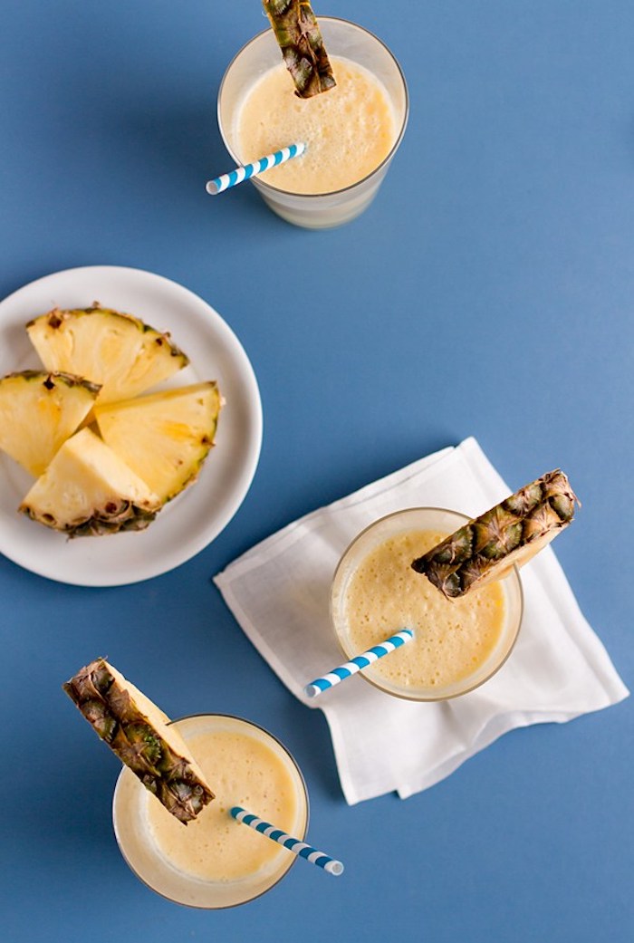 completed pineapple smoothie, poured into three glasses, each decorated with a pineapple slice, easy smoothie recipes, more pineapple chunks in a plate