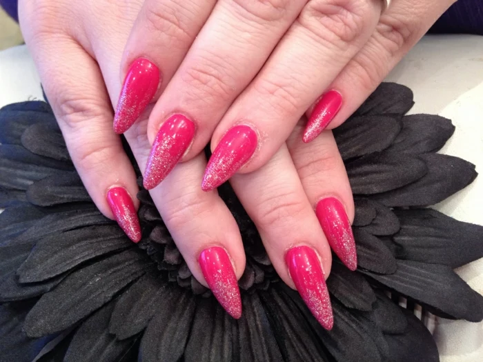 narrow and sharp claw nails, painted in red nail polish, and decorated with subtle silver glitter, on two hands, resting on black artificial flower
