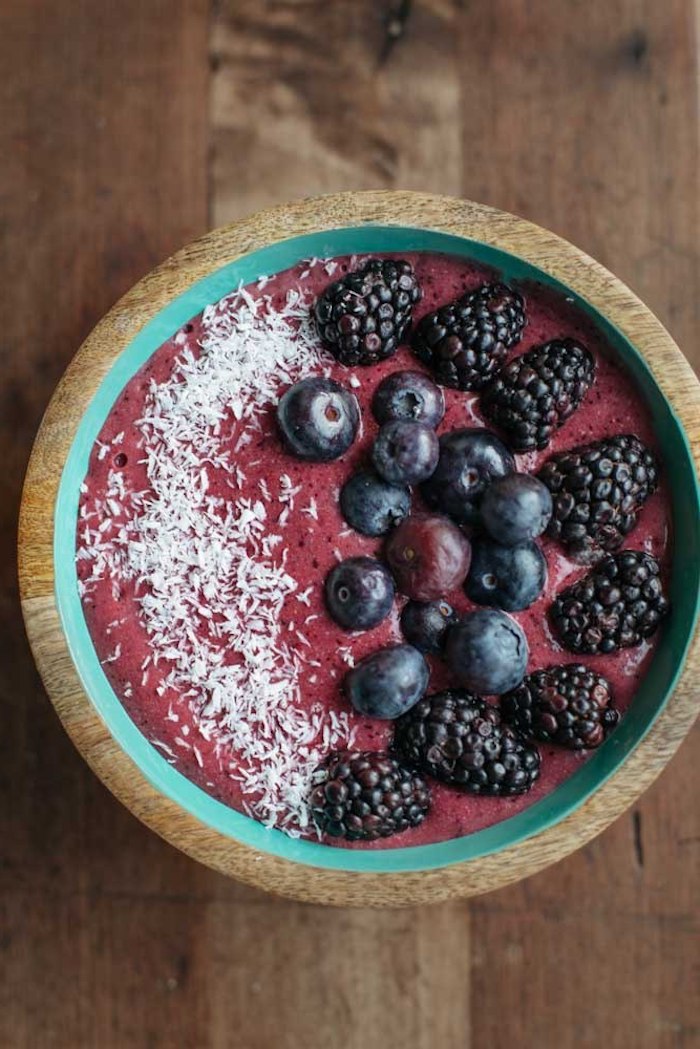 puree made from berries, inside a wooden turquoise bowl, healthy breakfast smoothies, topped with whole blueberries and blackberries, and a dusting of coconut shavings